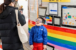 駅前地下道の壁面にテープアートの前で写真撮影をする親子